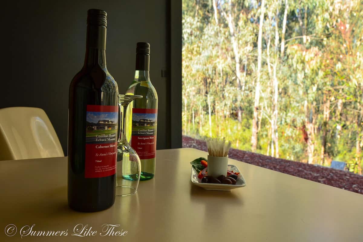 Dos botellas de vino y una copa sobre una mesa con un plato de uvas y aceitunas.