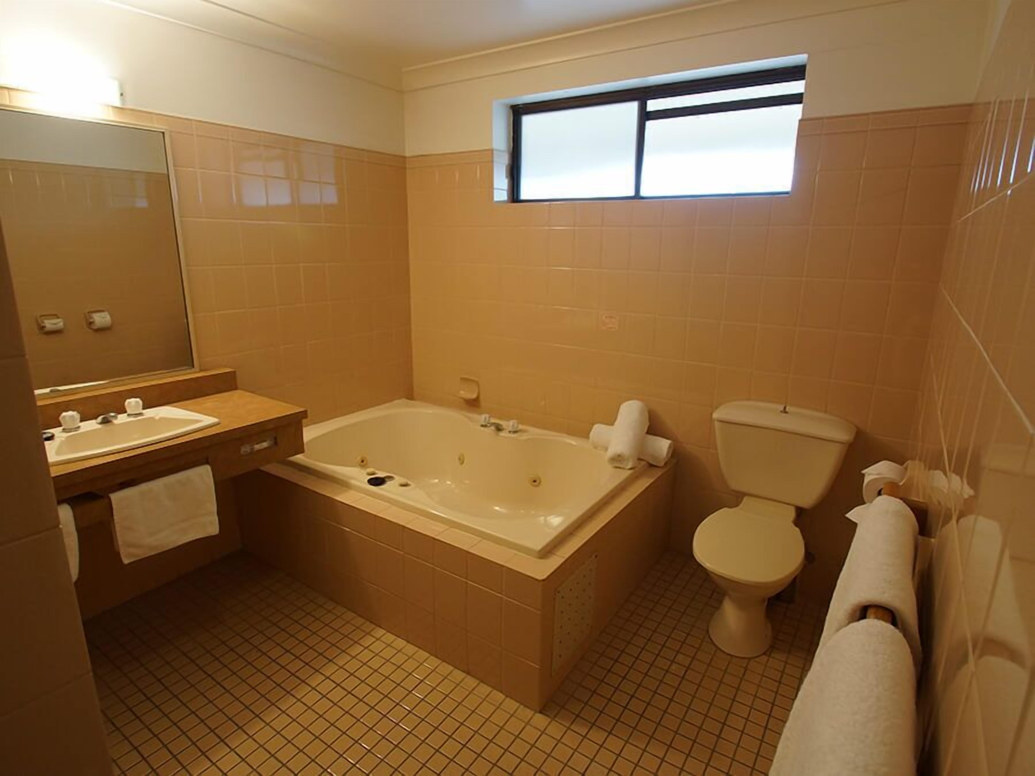 A bathroom with a bathtub, toilet, sink, and a window above the toilet.