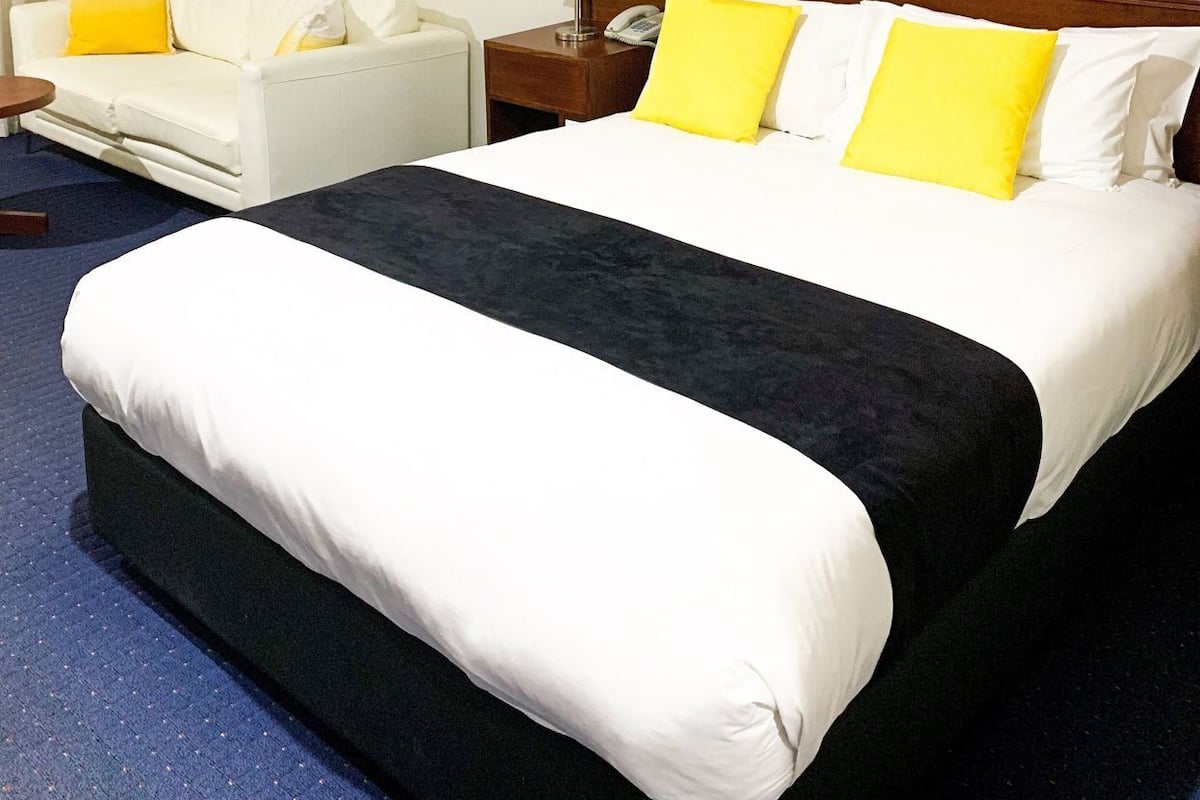 Una habitación de hotel con cama, una silla, una mesita de noche y una lámpara.
