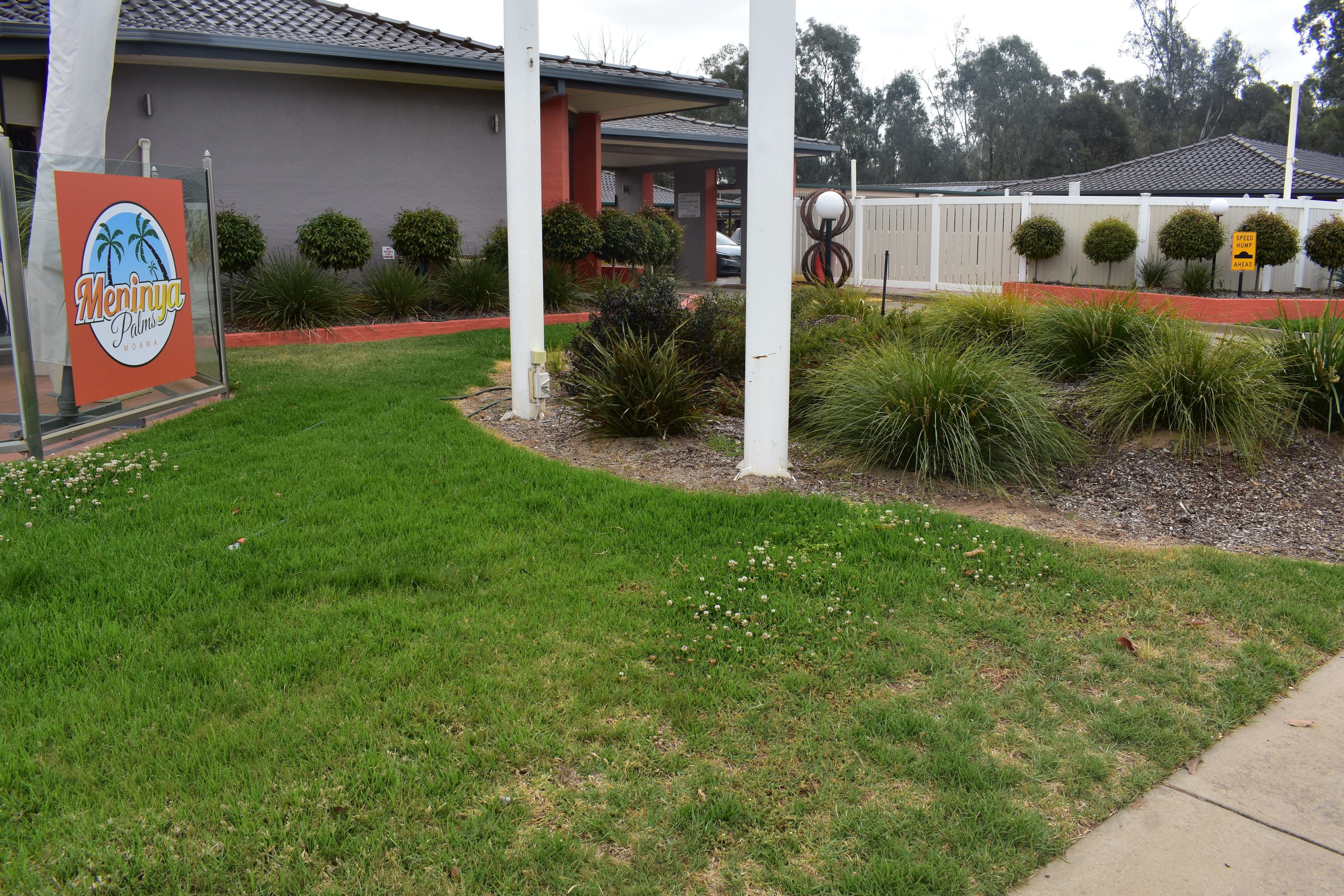 A hotel entrance with a sign, a covered patio, and well-maintained landscaping.