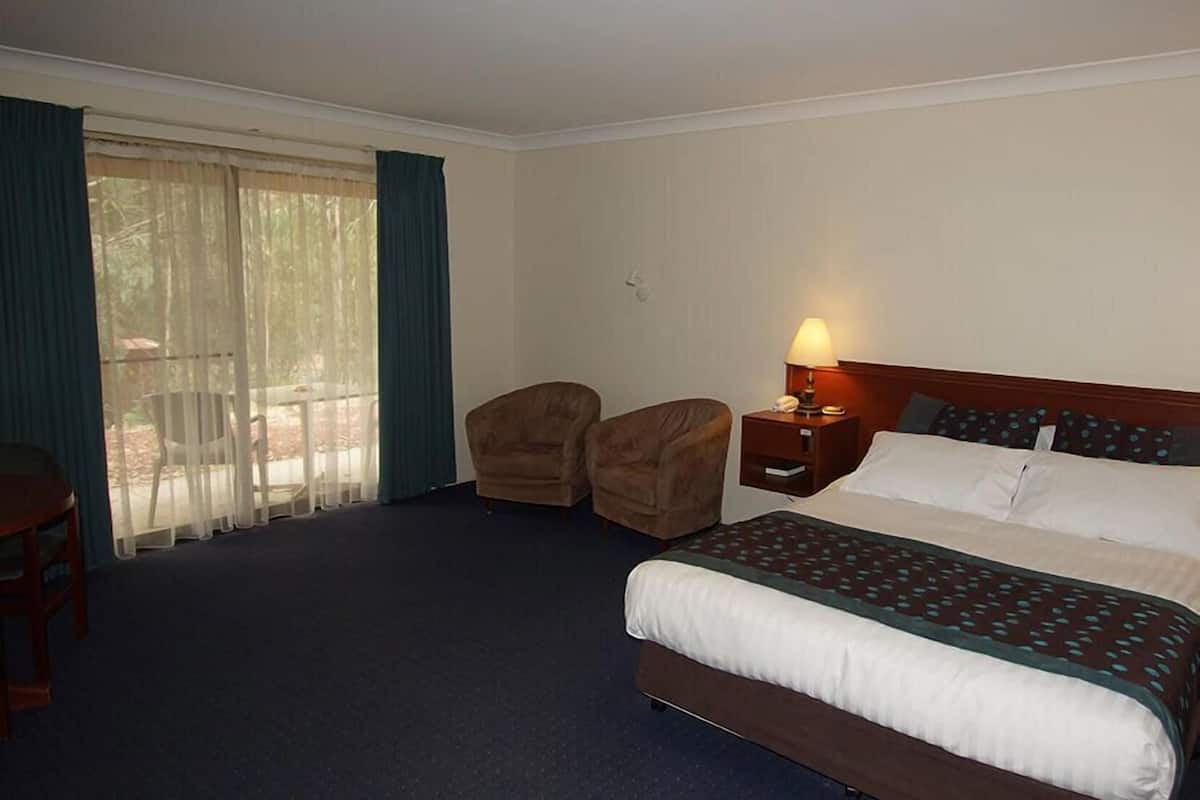 Una habitación de hotel con una cama, una mesita de noche, una silla y vistas al exterior a través de un ventanal grande.