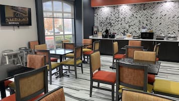 A dining area with multiple tables and chairs, a kitchen area with appliances, and a large window providing a view of the outside.