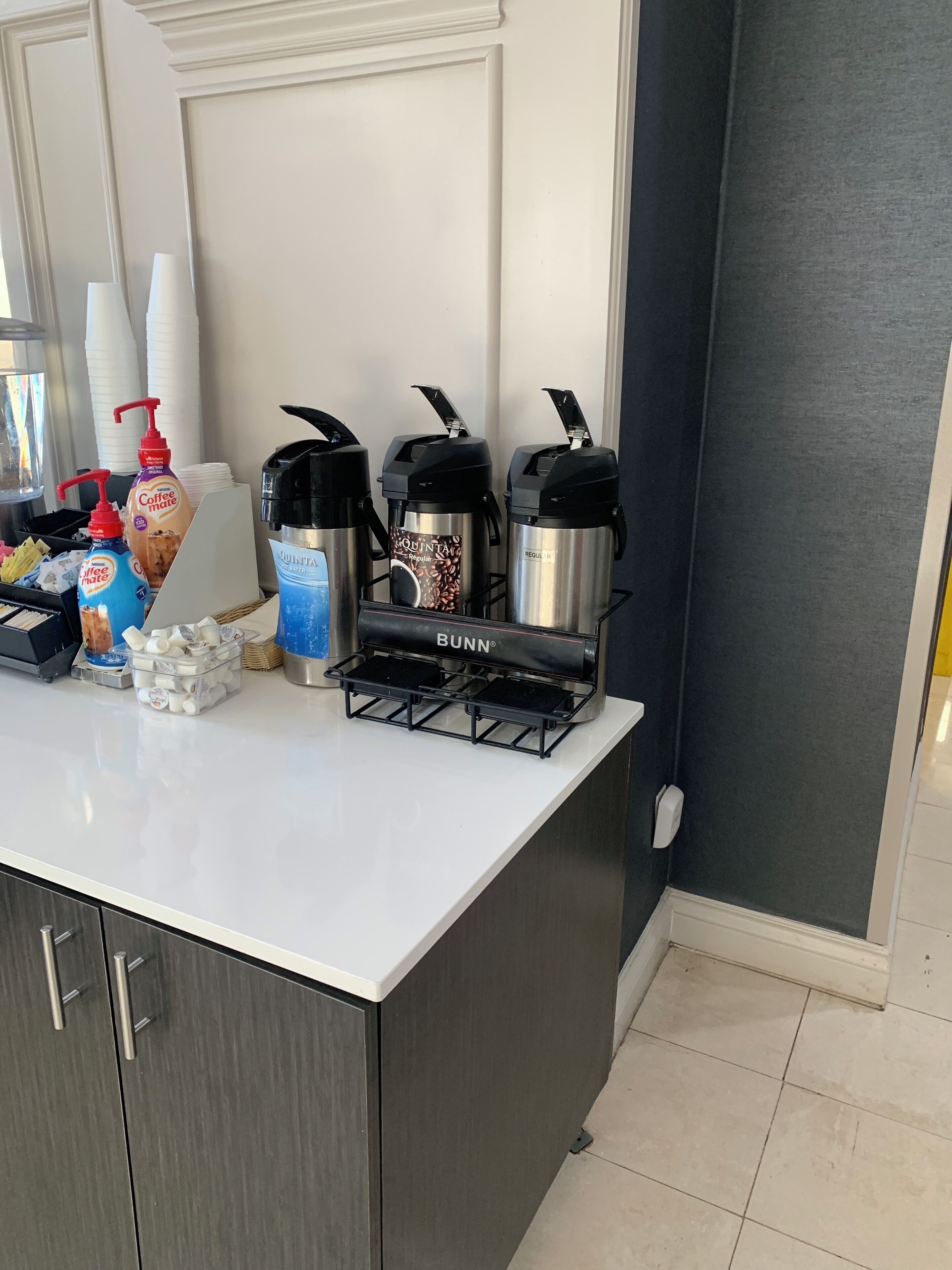 A kitchen counter with coffee makers, a coffee dispenser, and a Bunn coffee machine.