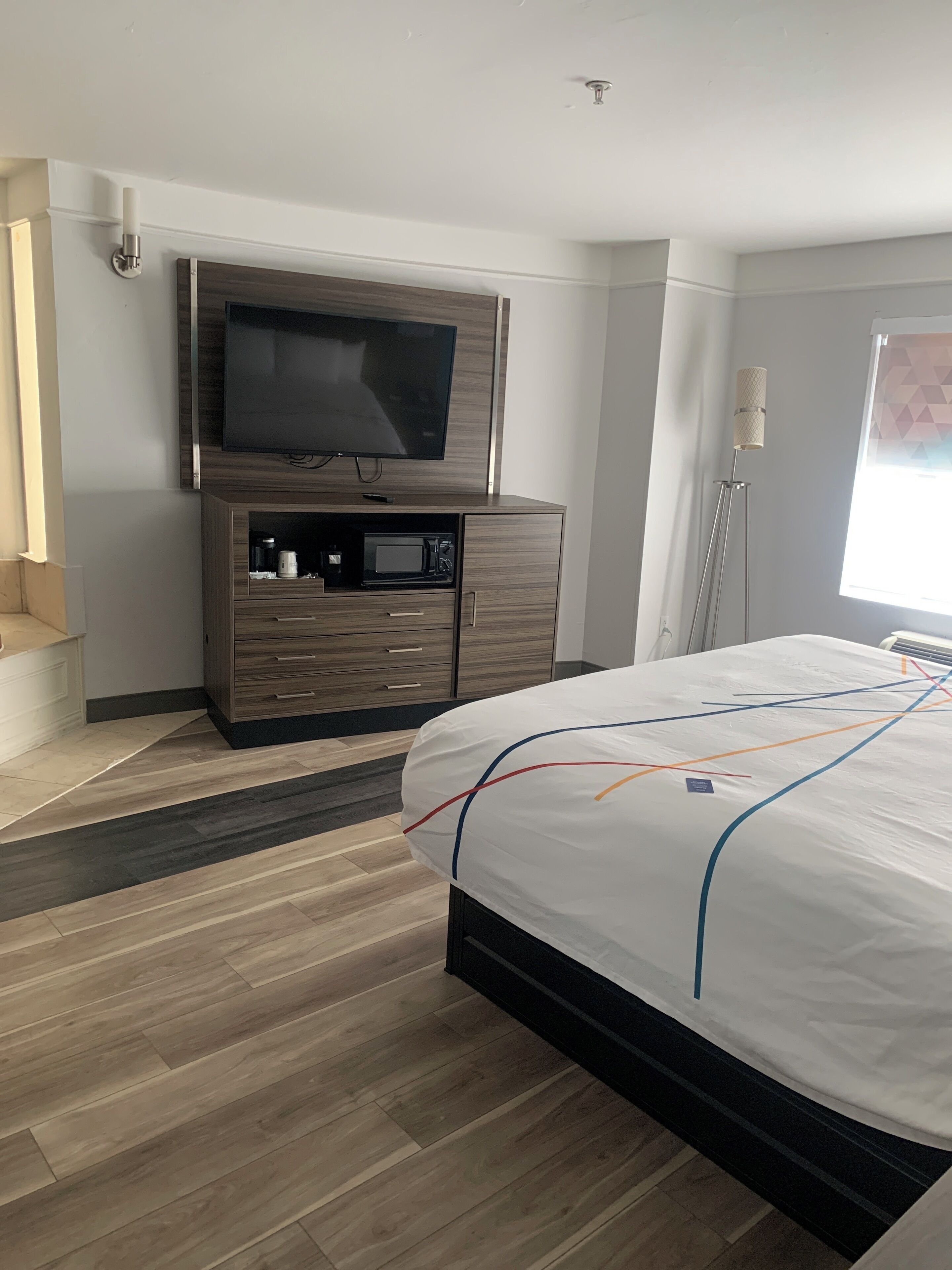 Une chambre d’hôtel moderne dotée d’un grand lit, d’un téléviseur à écran plat fixé à une armoire en bois, d’un four à micro-ondes et d’une table de chevet.