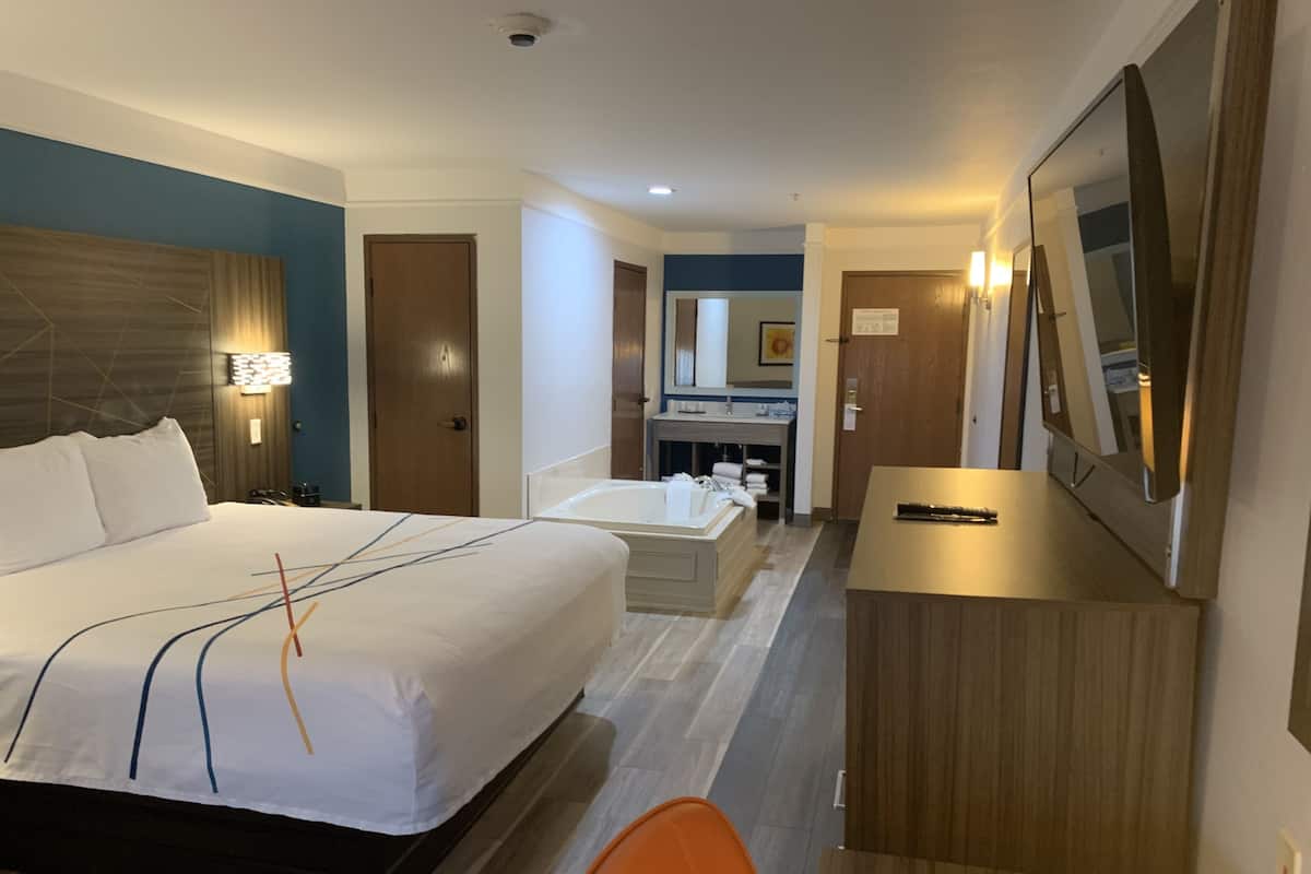 A hotel room with a large bed, a desk, a chair, a bathroom with a bathtub, and a mirror.