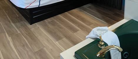 Una habitación de hotel moderna con una cama grande, mesitas de noche, una bañera verde y una pequeña kitchenette.