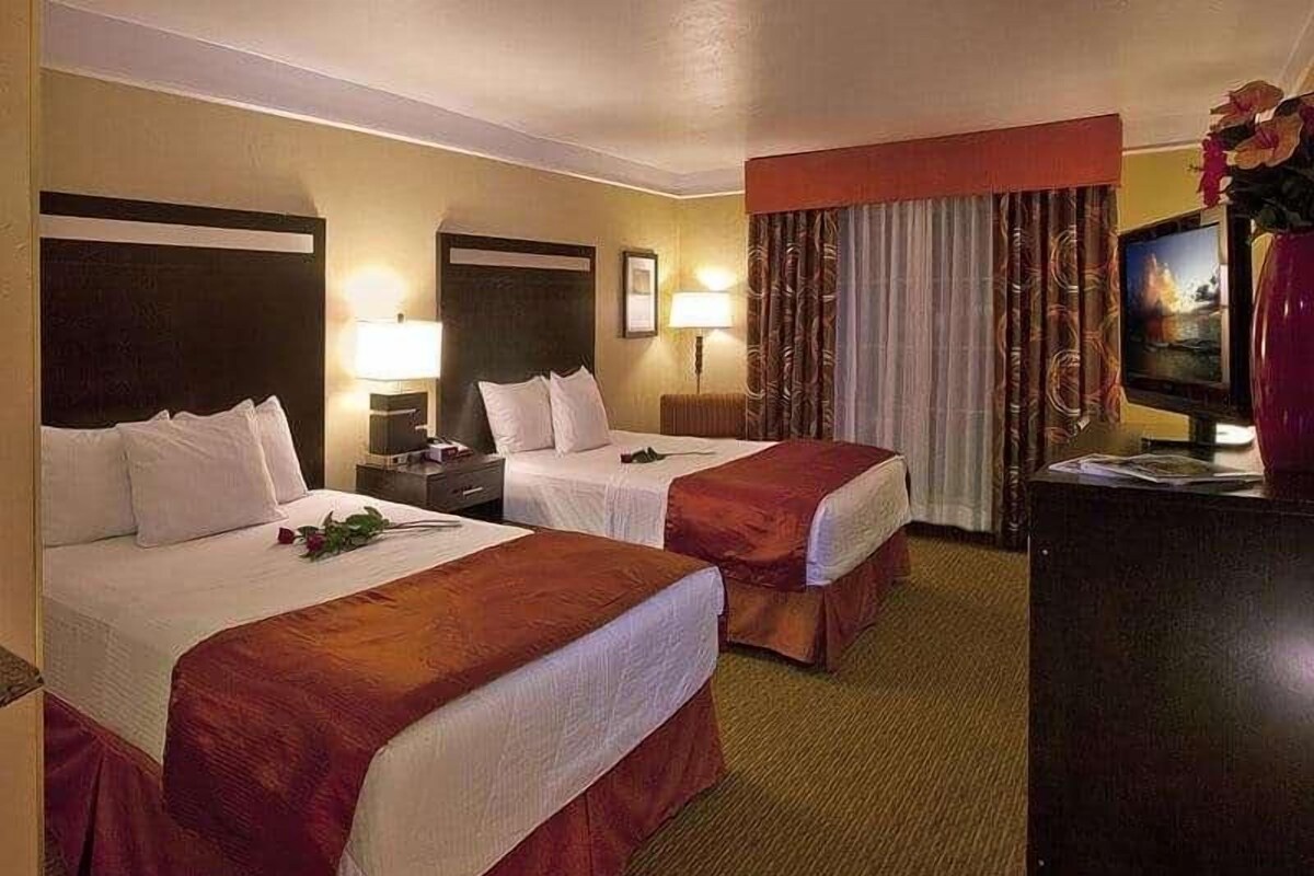 A hotel room with two beds, a TV, a desk, and a lamp.