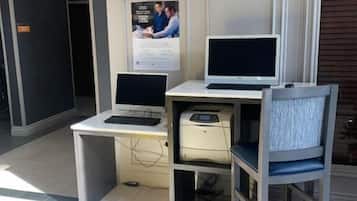A modern office space with two desks, one with a desktop computer and the other with a laptop. There is a printer on the desk, a chair, and a poster on the wall.