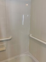 A corner of a room with a white bathtub, a white door, and a white handrail.