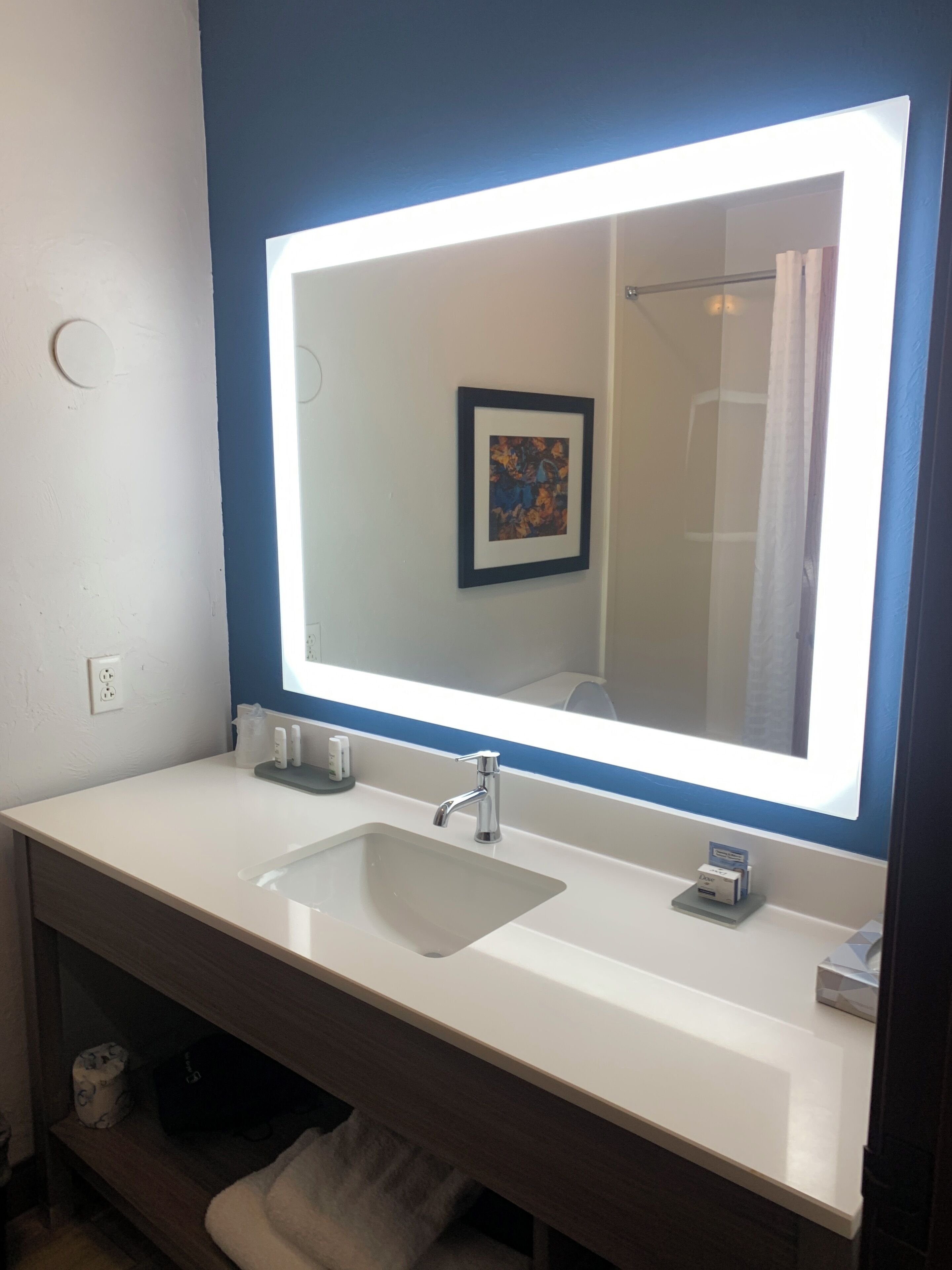 A bathroom with a white sink, a mirror with a light, and a towel rack.