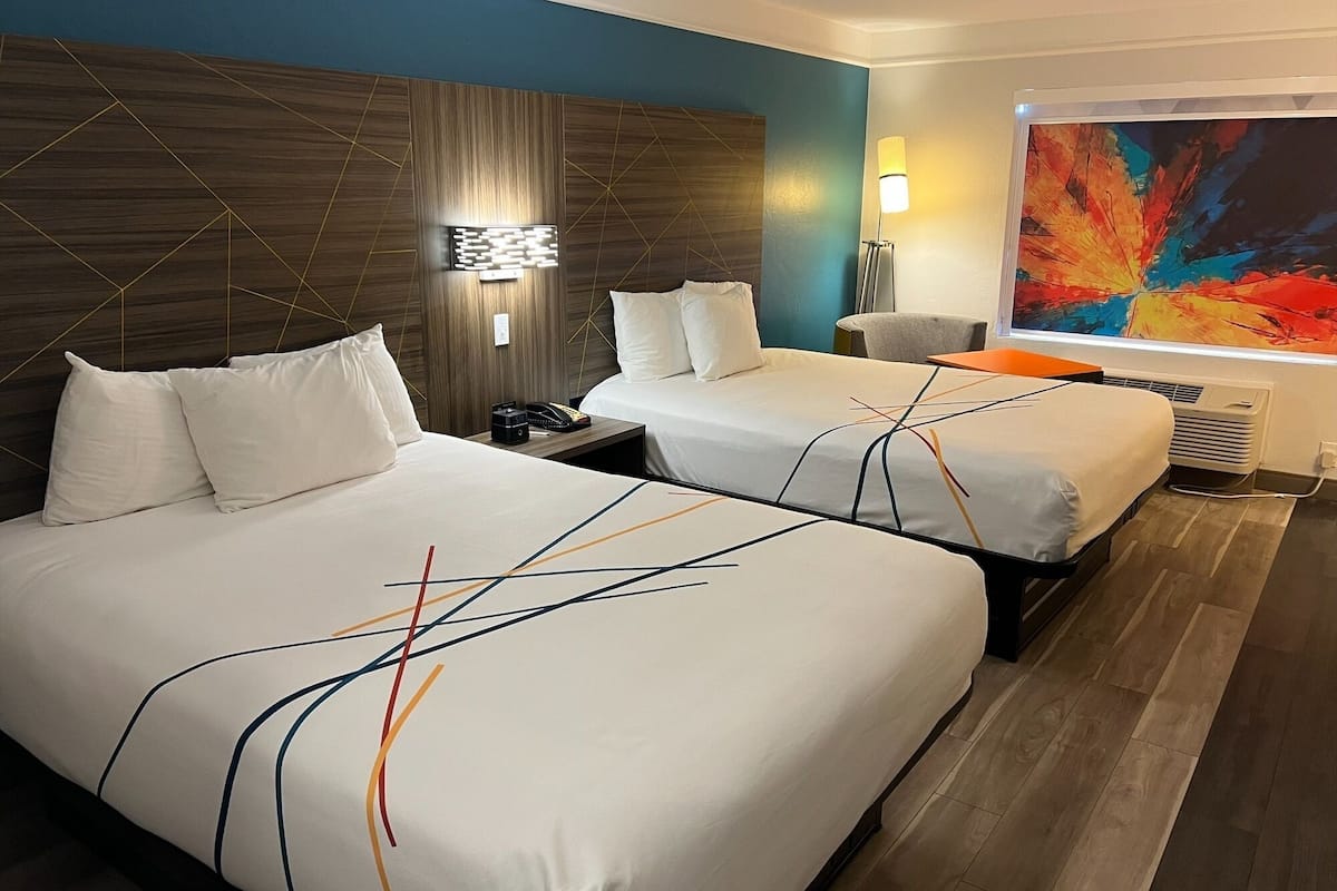 A hotel room with two beds, a modern headboard, a large abstract painting, and a floor lamp.
