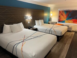 A hotel room with two beds, a modern headboard, a large abstract painting, and a floor lamp.