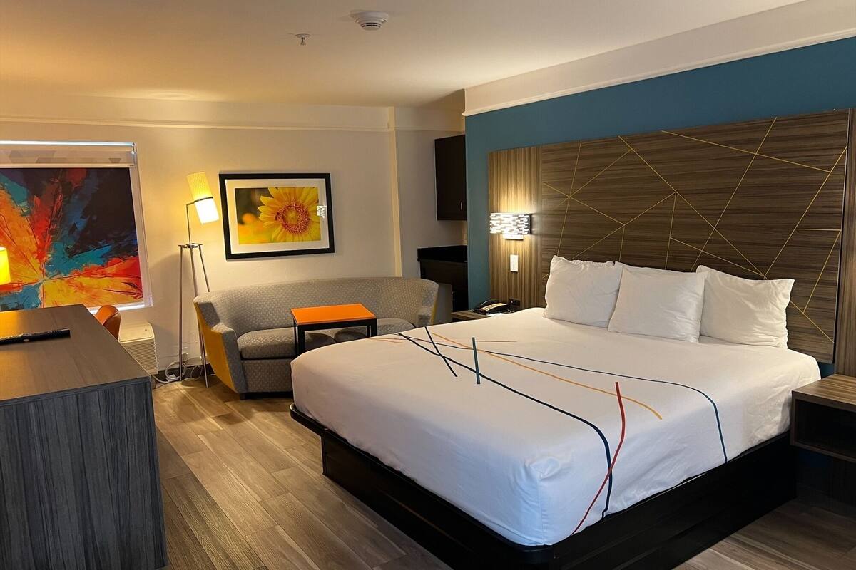 A hotel room with a large bed, a desk, a sofa, and a painting on the wall.