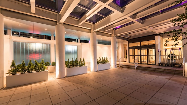 A spacious indoor area with large columns, potted plants, and a glass facade. - Hotel NoMa, Trademark Collection by Wyndham (New Rochelle)