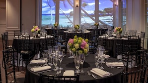 A banquet hall with round tables, black chairs, and floral centerpieces. - Hotel NoMa, Trademark Collection by Wyndham (New Rochelle)