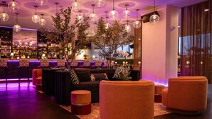 A modern lounge area with round seating, a bar in the background, and pendant lighting. - Hotel NoMa, Trademark Collection by Wyndham (New Rochelle)