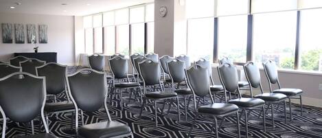 A conference room with rows of chairs, large windows, and a patterned carpet.