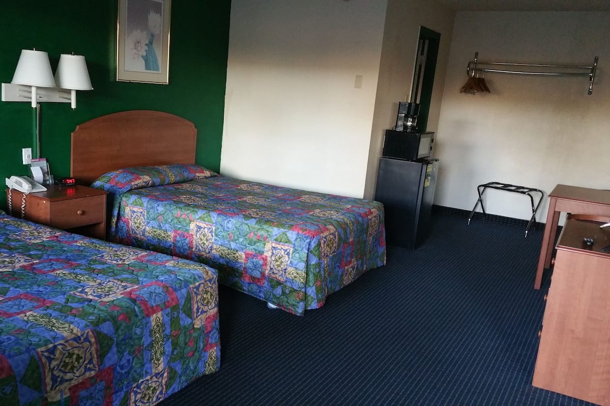 A hotel room with two beds, a desk, a refrigerator, a lamp, and a painting on the wall.