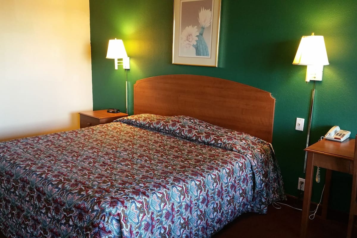 A hotel room with a bed, bedside lamps, a nightstand, a chair, and a phone on a table.