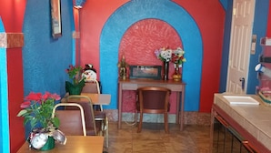 A restaurant with a vibrant color scheme, featuring red and blue walls, a tiled floor, and a central archway. There are tables and chairs, a counter with a sink, and decorative items like flowers and a statue. -  Stay Express Inn Near Downtown San Antonio TX (San Antonio)