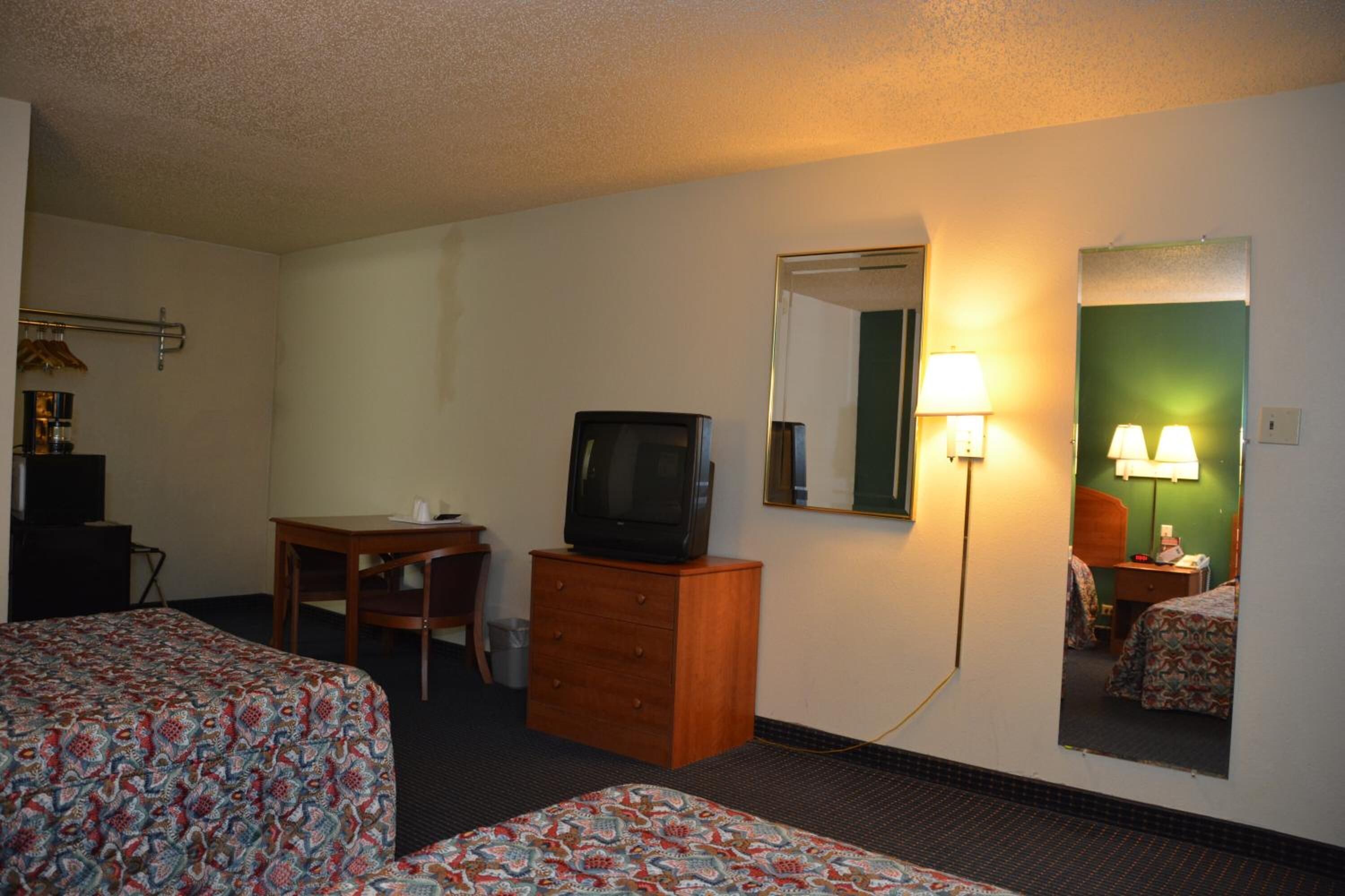 A hotel room with two beds, a desk with a television, a dresser, and a mirror.