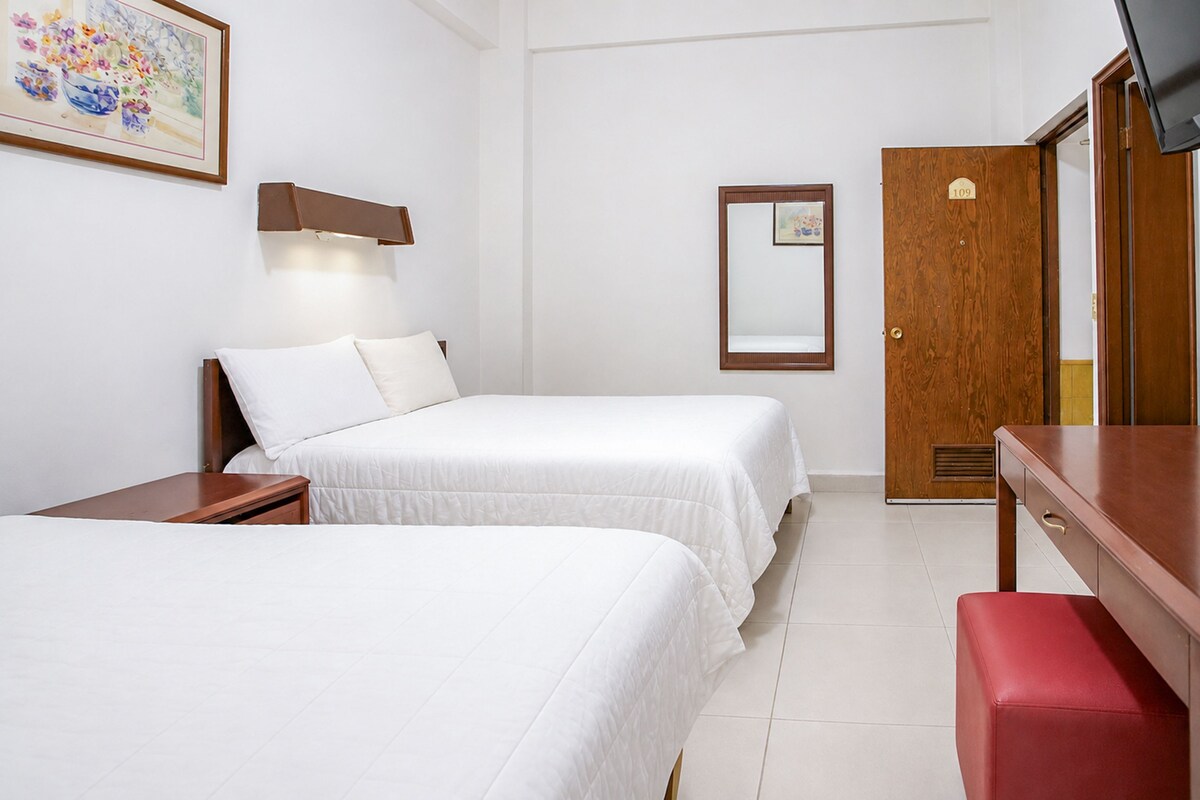 Une chambre d’hôtel avec deux lits, un bureau, une télévision et une porte.