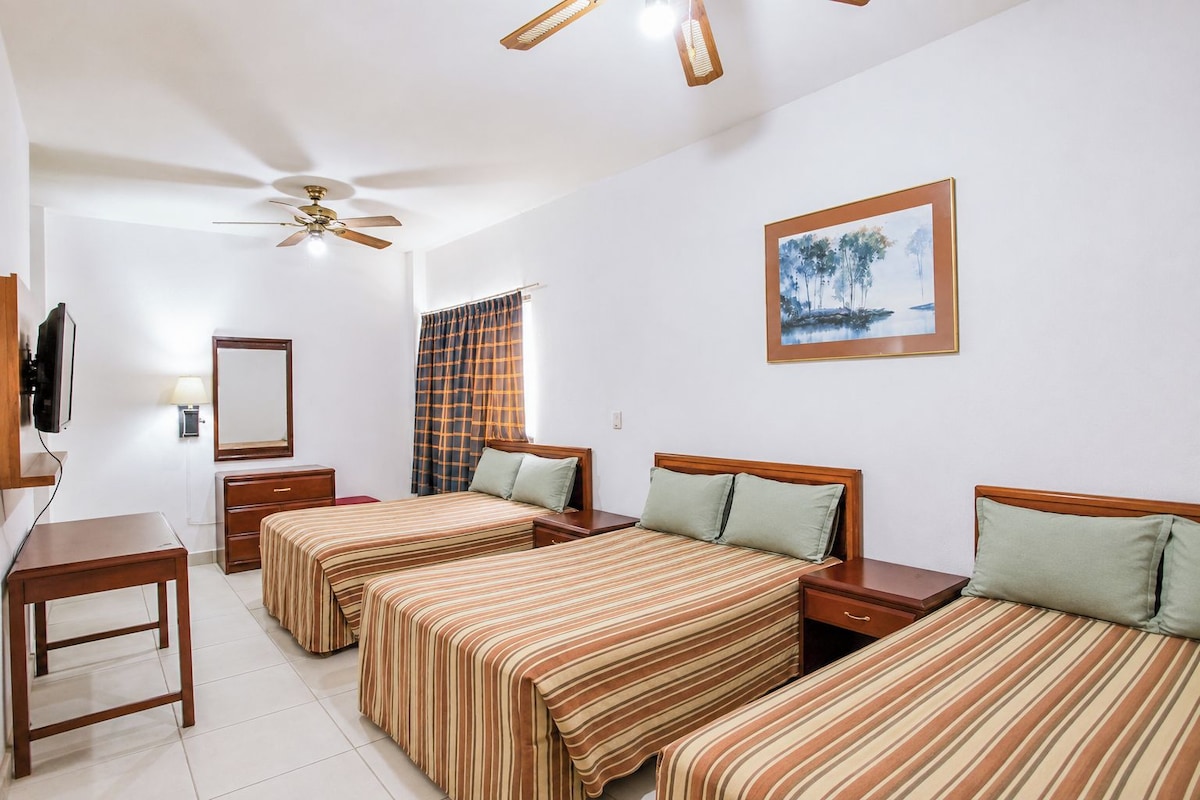 A hotel room with two beds, a desk, a TV, a ceiling fan, and a painting on the wall.