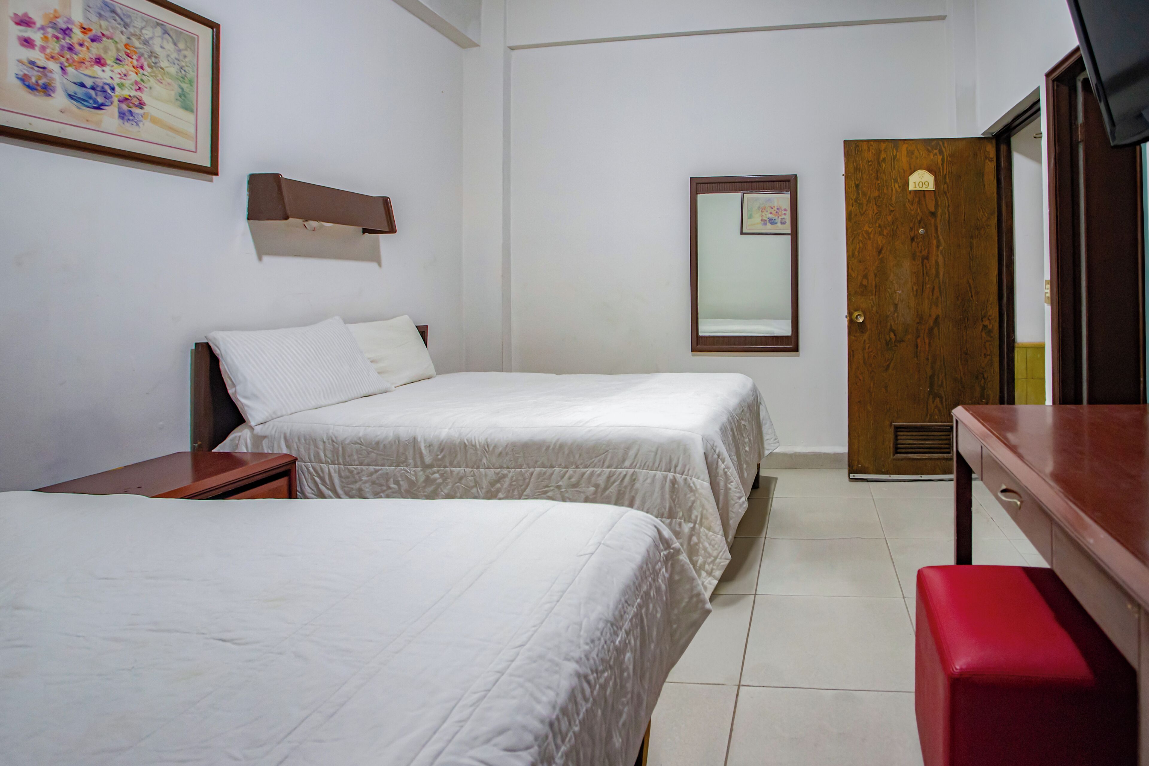 Een hotelkamer met twee bedden, een houten bureau, een spiegel en een deur met een nummer.