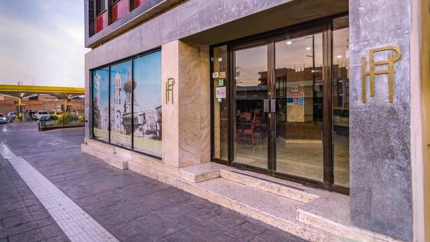 A hotel entrance with a large glass facade, a prominent 'R' logo, and a mural depicting a historical building. - Hotel Premier (Saltillo)