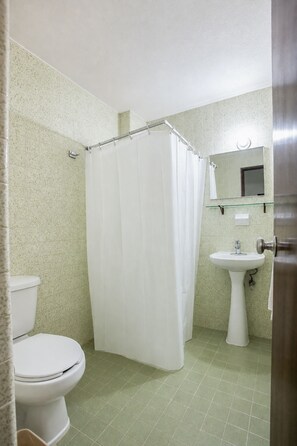 A bathroom with a toilet, a shower curtain, a sink, and a mirror. - Hotel Premier (Saltillo)