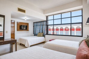 A hotel room with two beds, a TV, a desk, and a window with a view of a building with arches. - Hotel Premier (Saltillo)
