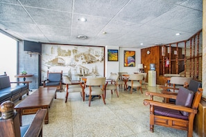 Un vestíbulo de hotel con techo alto, un mural grande en la pared, varias zonas de estar y una escalera de madera.