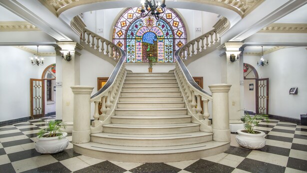 Una imponente escalera con un vitral en la parte superior, que lleva a una puerta con la inscripción "115-17".
