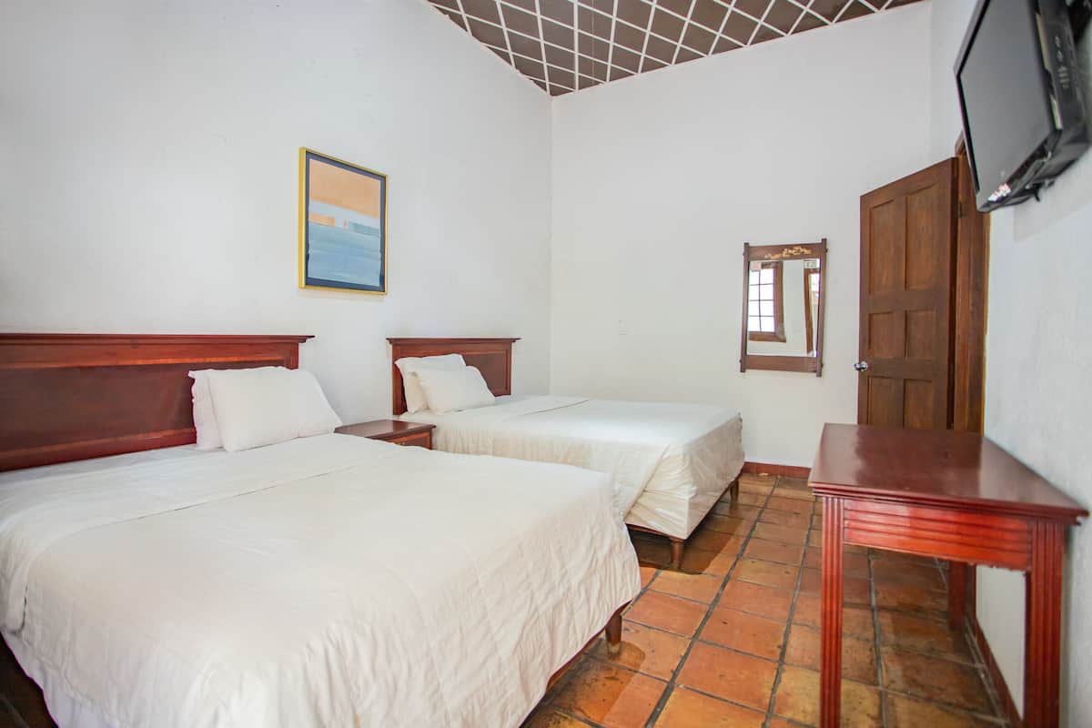 A hotel room with two beds, a wooden nightstand, a television, and a door.