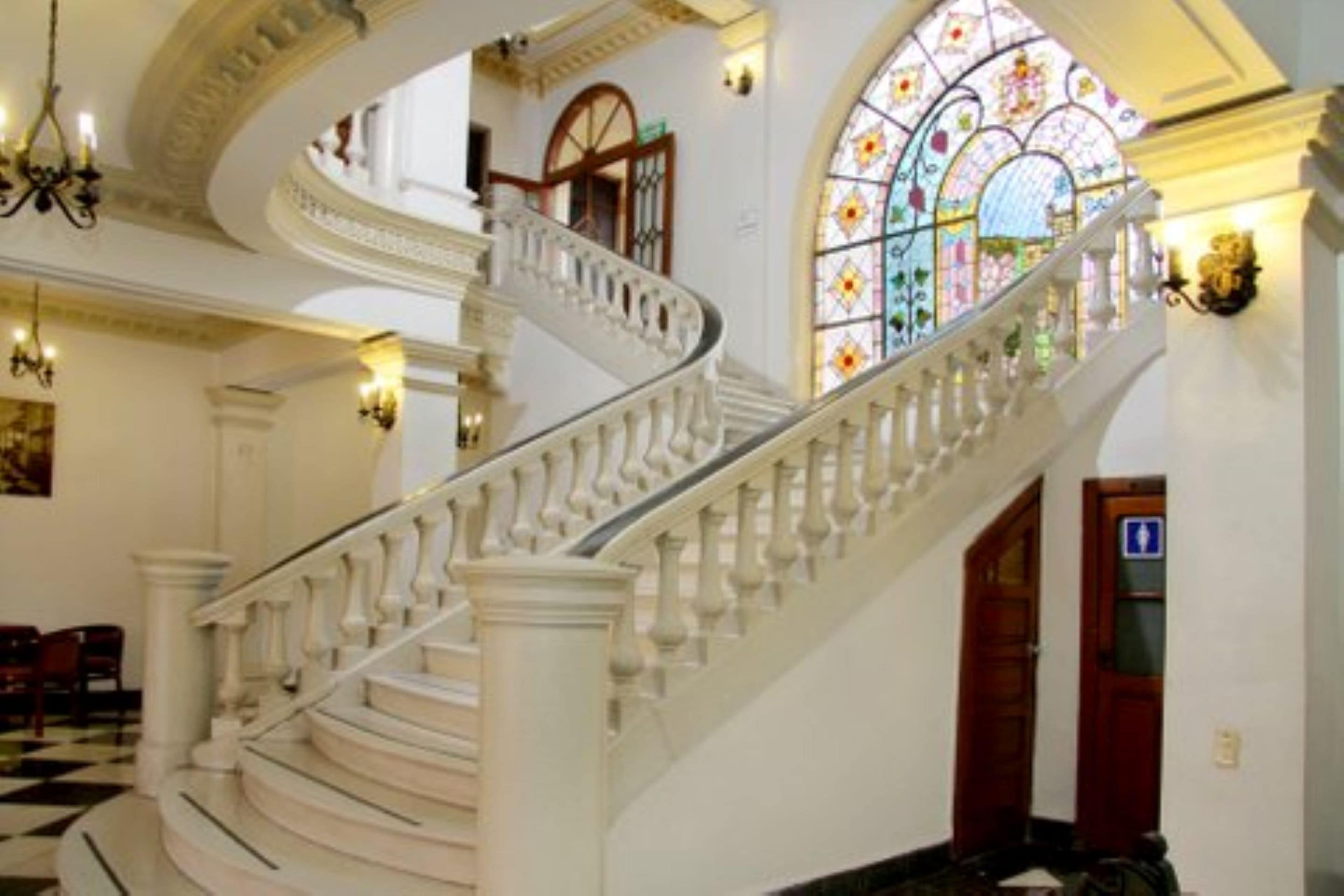 A grand staircase with ornate balustrades, leading to a second-floor landing with a large stained glass window.
