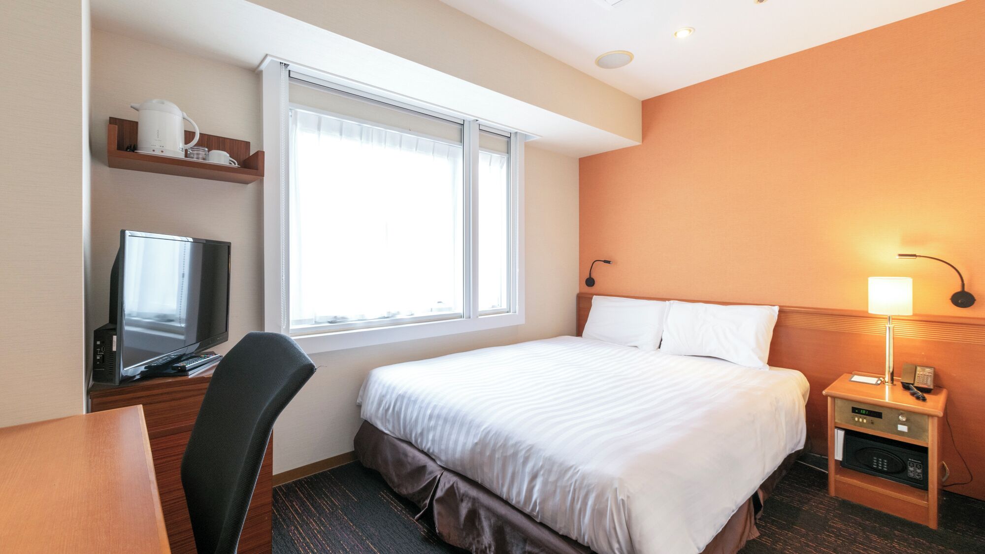 A hotel room with a bed, a desk with a computer, a TV, a lamp, and a microwave.