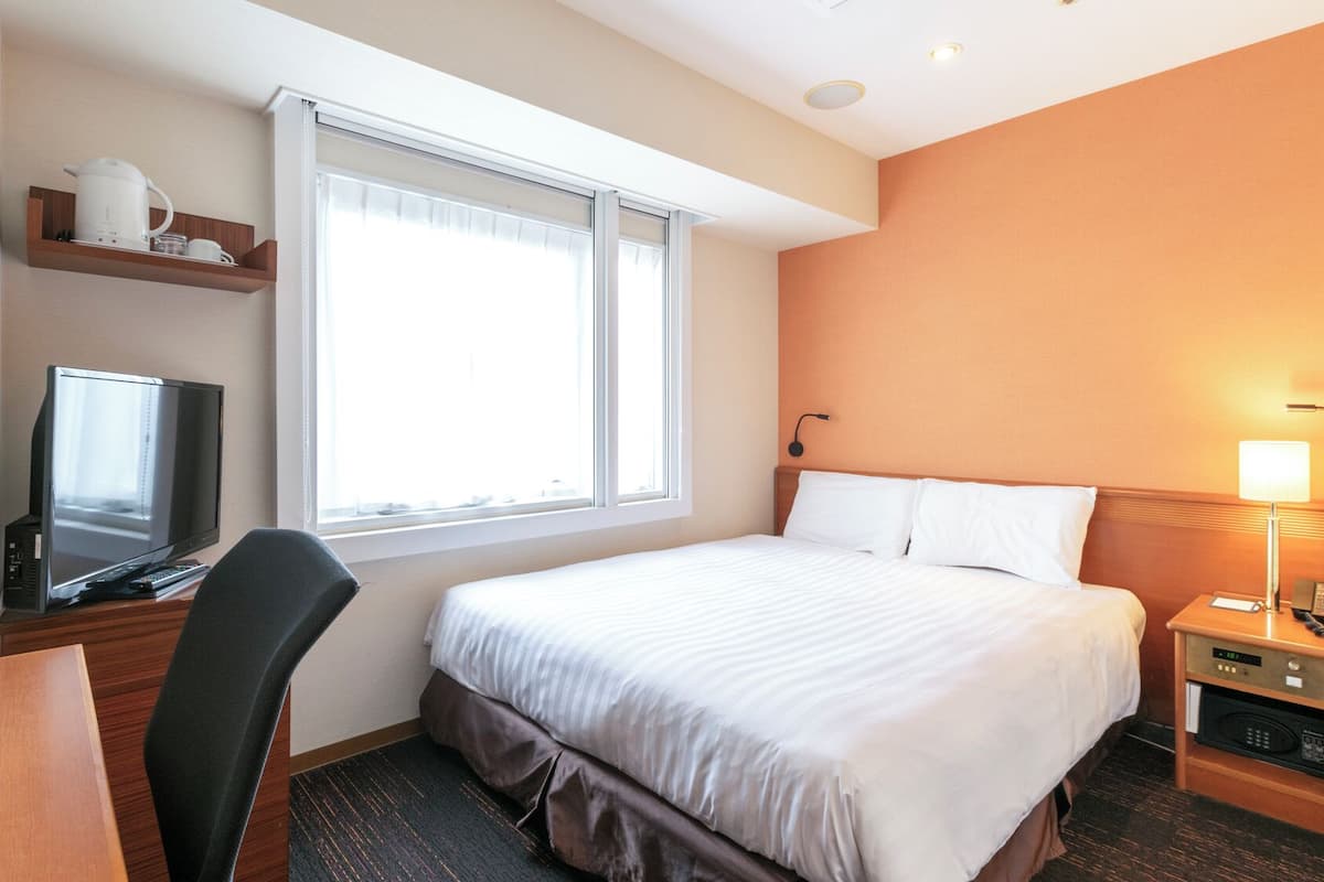 A hotel room with a bed, a desk with a computer, a TV, a lamp, and a microwave.