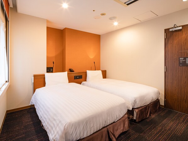 A hotel room with two beds, a wooden wardrobe, and a wall-mounted phone.