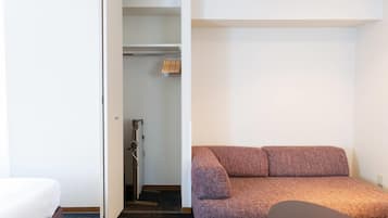Una habitación pequeña con una cama, un sofá marrón y un armario con ropa colgada.