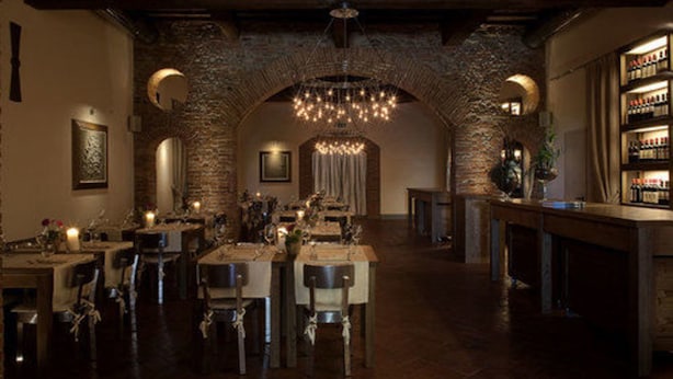 A dimly lit restaurant with brick arches, wooden tables, and a chandelier.