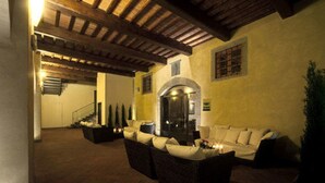 An outdoor living area with a fireplace, sofas, and a staircase leading to an upper floor.