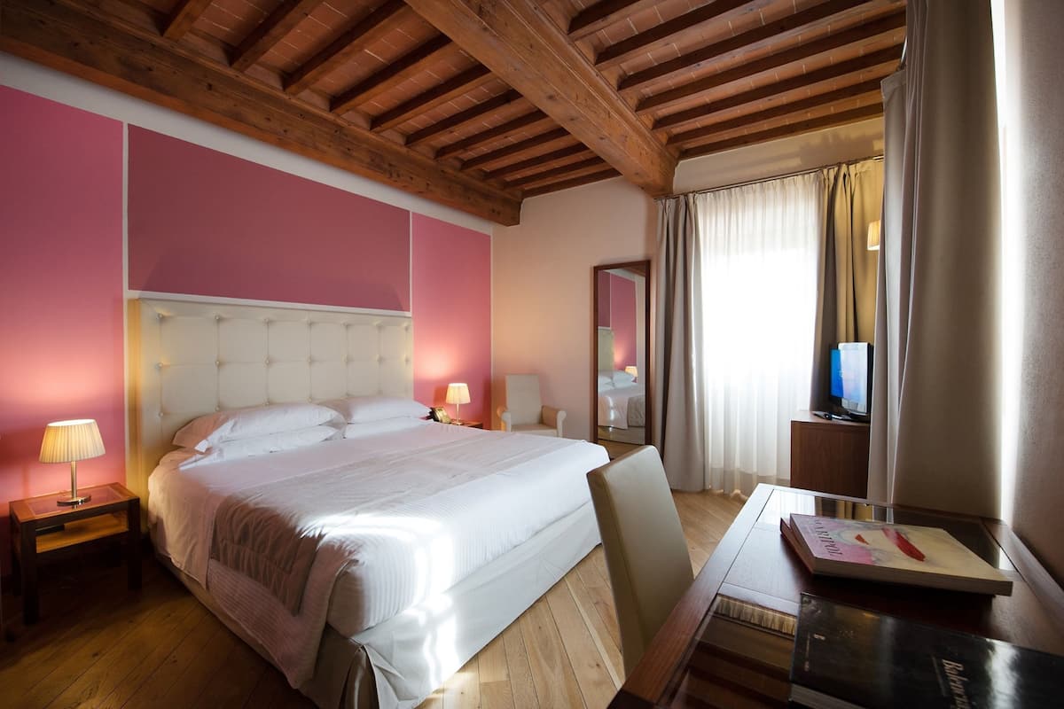 Habitación de hotel con una cama grande, vigas de madera en el techo, un televisor y un escritorio con un libro.