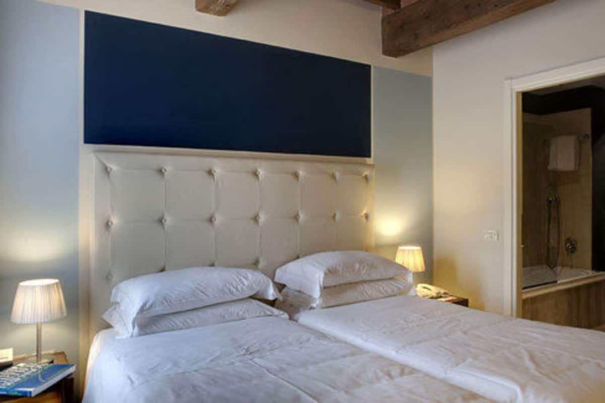 Una cama doble con cabecera capitonada, una lámpara de noche y una mesita de noche con un libro.