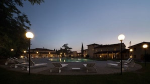 A pool area with lounge chairs and street lamps, surrounded by buildings.