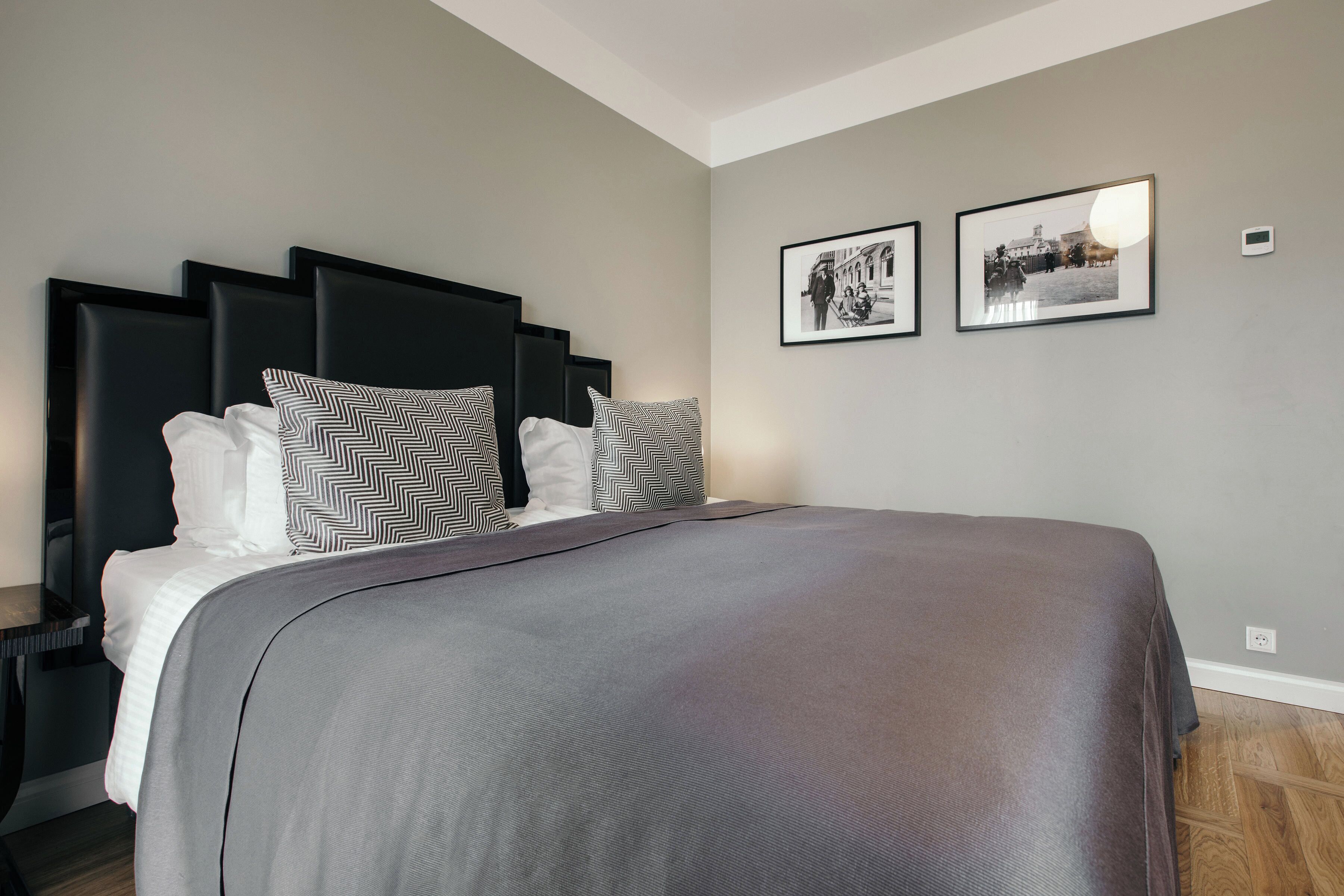 A modern bedroom with a large bed, black headboard, and two framed pictures on the wall.