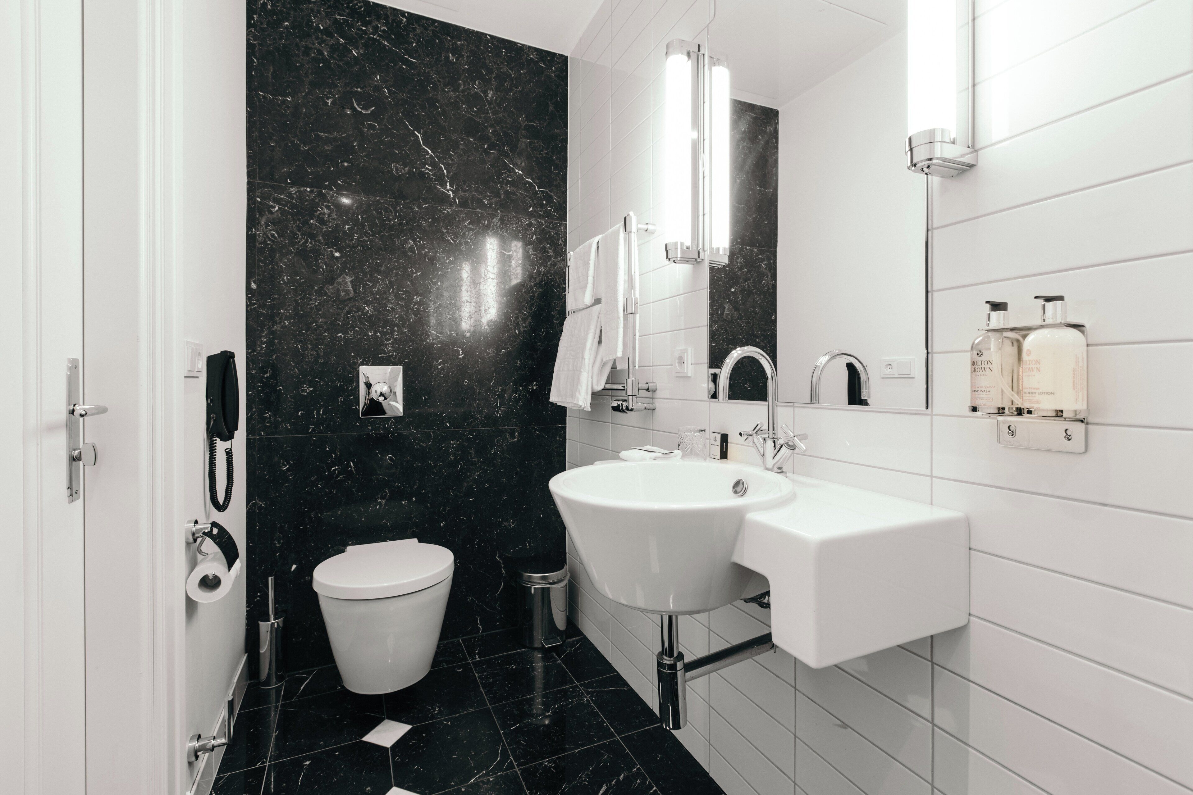 A modern bathroom with a white sink, a toilet, and a black marble wall.