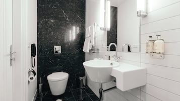 Un baño moderno con un lavamanos blanco, un inodoro y una pared de mármol negro.