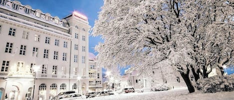 A snow-covered building with multiple windows and a tree in the foreground.