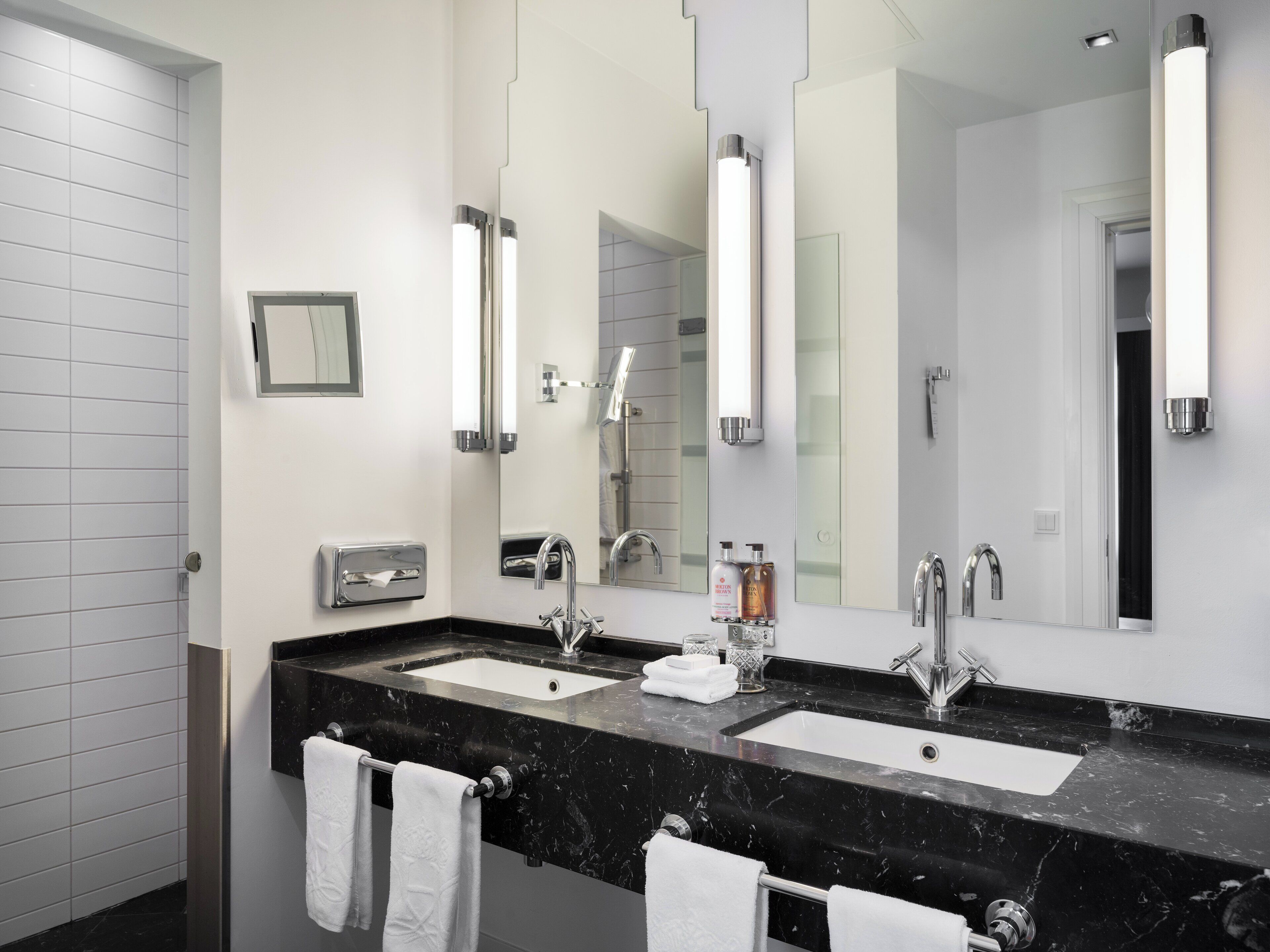 A modern bathroom with two sinks, a large mirror, and a towel rack.