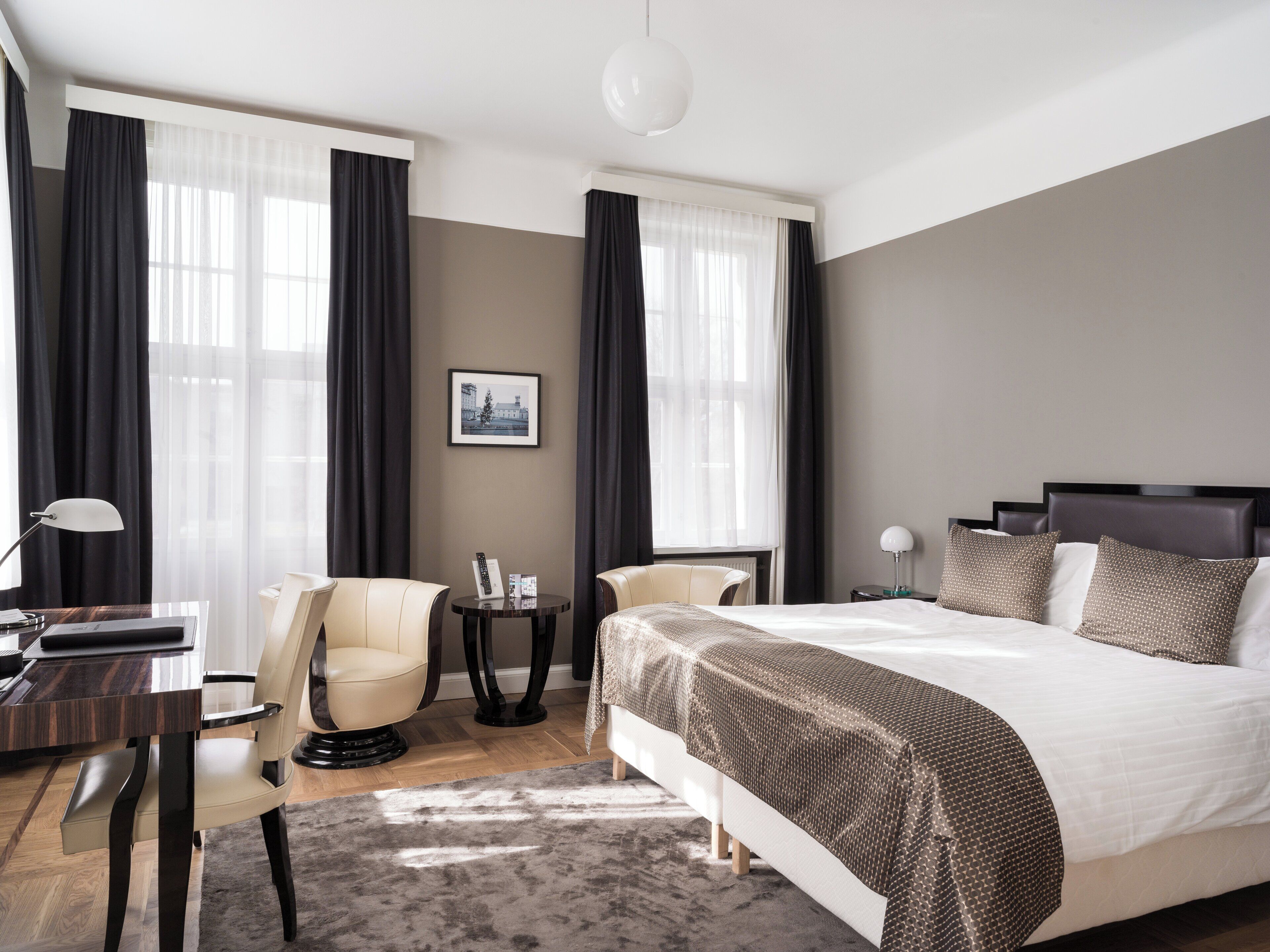 A modern hotel room with a large bed, two chairs, a small table, and a desk.
